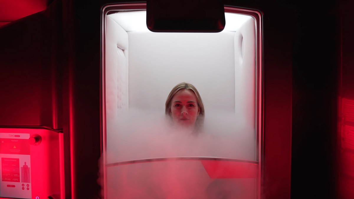 A woman inside a cryotherapy chamber surrounded by cold mist, with red ambient lighting